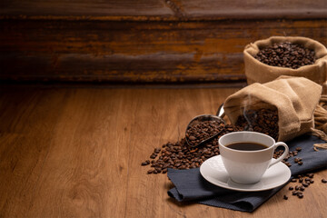 coffeeHot coffee in a white coffee cup and many coffee beans placed around on a wooden table in a warm, light atmosphere, on dark background.