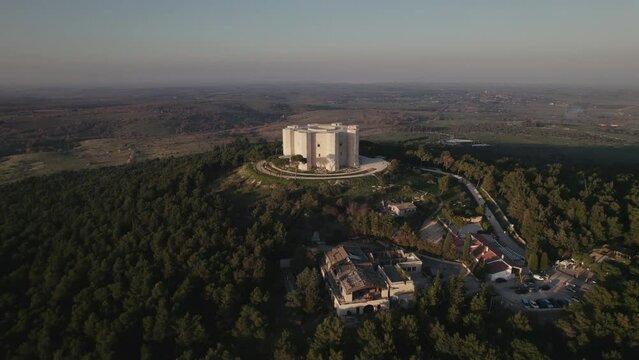 Aerial of a white 13th century Italian citadel on top of a hill and green forest in Puglia, Italy 4K drone