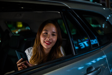 Fototapeta na wymiar Asian businesswoman commuting from office in Taxi backseat with mobile phone on road in city at night after late work, Beautiful woman using smartphone sitting back seat her car in urban