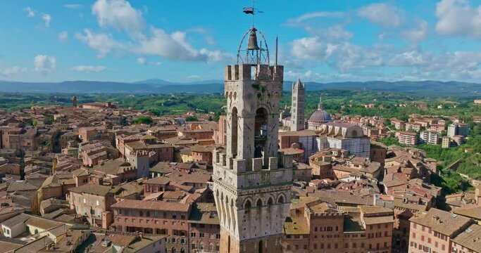 Aerial around the bell tower of the Torre del Mangia (Mangia Tower) and the surrounding old city of Siena, Tuscany, Italy. Drone orbit shot