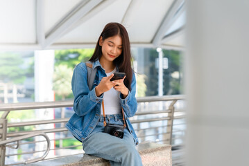 Young asian woman using mobile in city. Happy female tourist wearing jeans jacket and holding smartphone at public