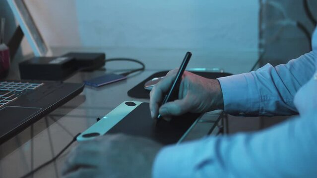 Man drawing with pen on a digital graphic tablet working as a designer. Vector design work from modern home office. Professional  freelance worker on the laptop computer.
