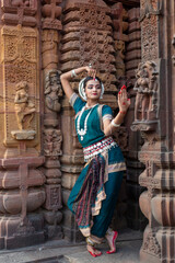 Indian classical odissi dancer pose against the backdrop of temple with sculptures