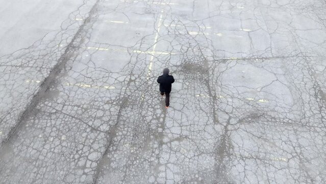 Man walking in a downtown Lansing, Michigan parking lot with drone video following above.