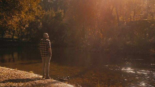 Mustached man in blue shirt leaves riverbank after admiring golden sunlight and trees. Relaxing and warm nature footage.