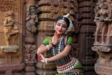 Beautiful Odissi Dancer posing in front of temple  sculptures in bhubaneswar, Odisha, India.