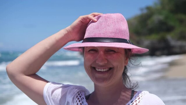 An elegant tourist in a white summer dress and a pink hat, strolling along a tropical beach on a sunny day on the ocean.