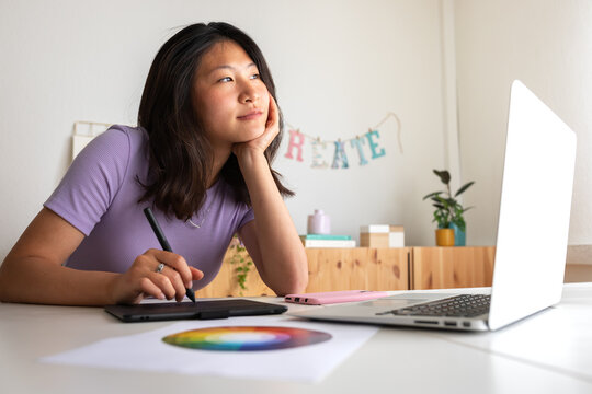 Asian young female graphic design student working on a project at home using tablet and laptop. Color wheel. - Powered by Adobe