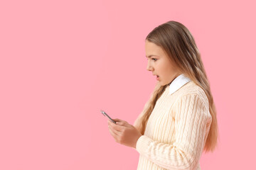 Fototapeta premium Shocked little girl using mobile phone on pink background