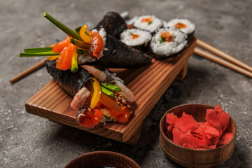 Wooden board with tasty sushi cones, rolls and ginger on grunge background, closeup