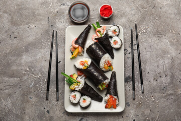 Plate with tasty sushi cones, rolls, soy sauce, ginger and chopsticks on grunge background