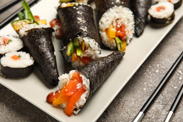 Plate with tasty sushi cones and rolls on grunge background, closeup