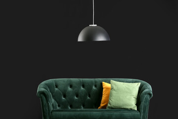Stylish green sofa with cushions and lamp on black background