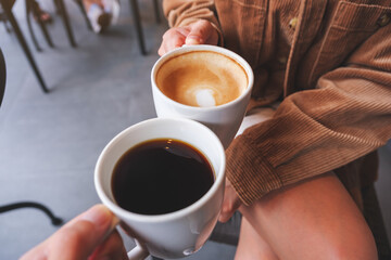 Closeup image of a couple people clinking white coffee mugs in cafe