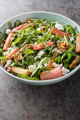 Fresh salad with rhubarb, arugula, goat cheese and walnuts close-up in a bowl on the table. Vertical