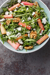 Rhubarb salad with arugula, goat cheese and walnuts close-up in a bowl on the table. Vertical top view from above
