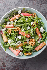 Fresh salad with rhubarb, arugula, goat cheese and walnuts close-up in a bowl on the table. Vertical top view from above