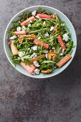 Salad with baked rhubarb, arugula, goat cheese and walnuts with honey dressing close-up in a bowl on the table. Vertical top view from above
