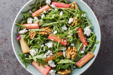 Homemade mix salad with baked rhubarb, arugula, goat cheese and walnuts close-up in a bowl on the table. Horizontal top view from above