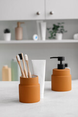 Holder of bamboo toothbrushes, soap and paste on white table in room