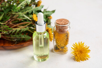 Bottles with cosmetic oil and plate of dandelion flowers on white background