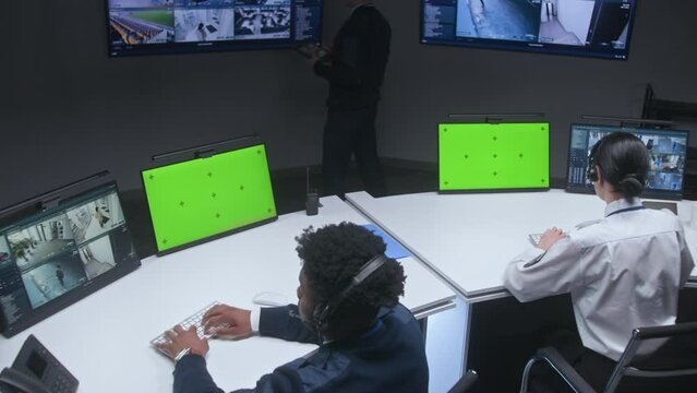 Multi ethnic officers and operators control CCTV cameras. Employees work in security control center. Big digital screens and computer monitors showing surveillance cameras video footage. Green screen.