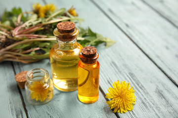 Bottles with cosmetic oil and dandelion flowers on blue wooden background