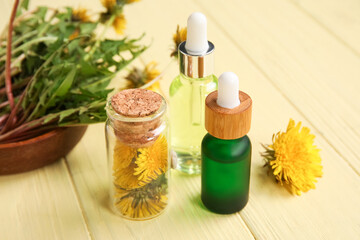 Bottles with cosmetic oil and bowl of dandelion flowers on yellow wooden background