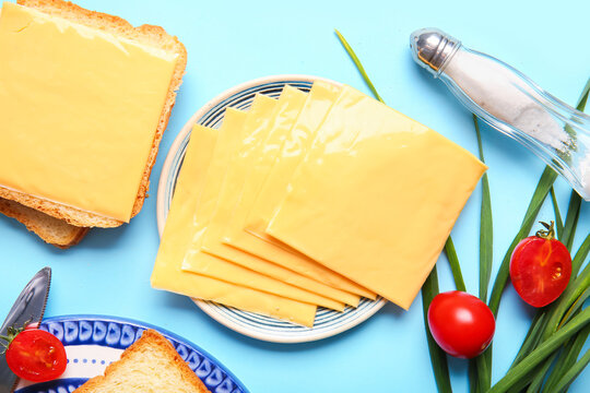 Plates of tasty processed cheese with bread and vegetables on blue background