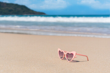 Fototapeta na wymiar Pink color sunglasses in heart shape on sandy beach at tropical seaside on warm sunny day. Summer vacation concept. Copy space, close up