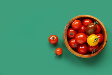 Bowl with different fresh tomatoes on green background