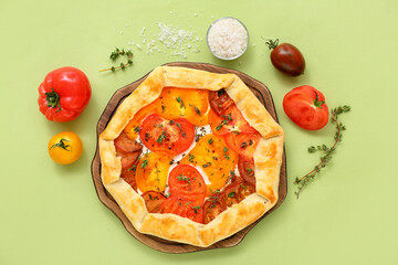Board with tasty tomato galette on green background