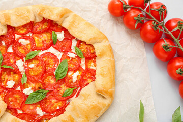 Baking paper with tasty tomato galette and basil on table