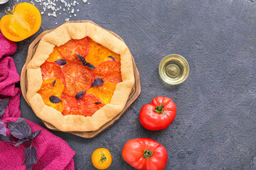 Board with tasty tomato galette and basil on dark background