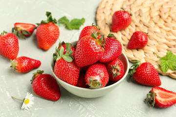 Bowl of fresh strawberries with leaves and chamomile flower on grey background