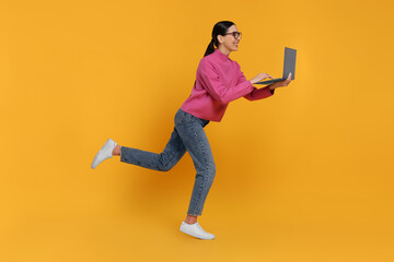 Fototapeta na wymiar Happy woman with laptop running on orange background