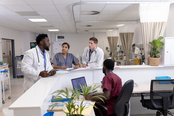 Diverse doctors and medical staff talking at reception desk of hospital ward