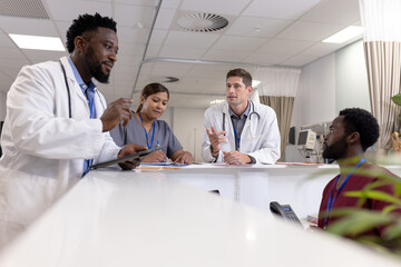 Fototapeta premium Busy diverse doctors and medical staff talking at reception desk of hospital ward, copy space