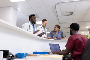 Busy diverse doctors and medical staff talking at reception desk of hospital ward, copy space