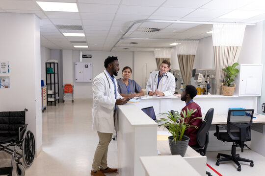 Happy diverse doctors and medical staff talking at reception desk of hospital ward, copy space