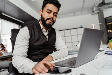 Young indian brunette man wearing suit working on laptop sitting in office