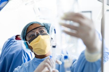 Asian female surgeon checking drip bag during surgery in operating theatre