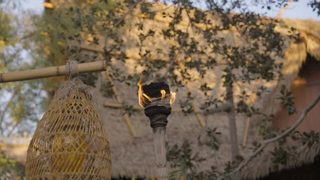 This video shows a tiki torch burning in slow motion with a thatched Polynesian hut background.