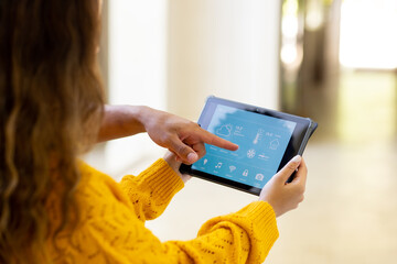 Diverse couple at home, woman holding tablet and man pointing to smart home interface on screen