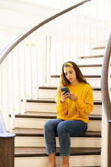 Thoughtful caucasian woman sitting on stairs at home using smartphone, with copy space