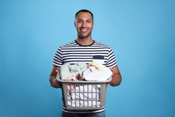 Happy man with basket full of laundry on light blue background