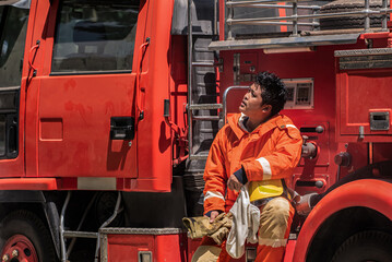 Firefighter sitting on fire truck and looking to the top with exhausted from fight a blaze and save...