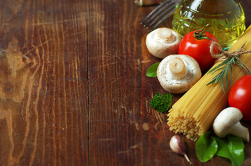 Spaghetti, tomatoes, olive oil, mushrooms and herbs on an old wooden table. Italian cuisine. Dark background.
