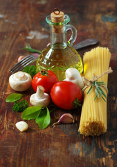 Spaghetti, tomatoes, olive oil, mushrooms and herbs on an old wooden table. Italian cuisine. Dark background.
