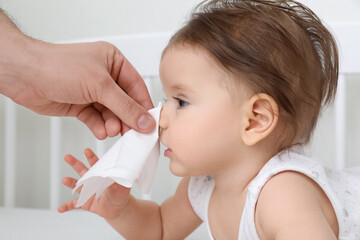 Father wiping runny nose of little baby with napkin on bed, closeup
